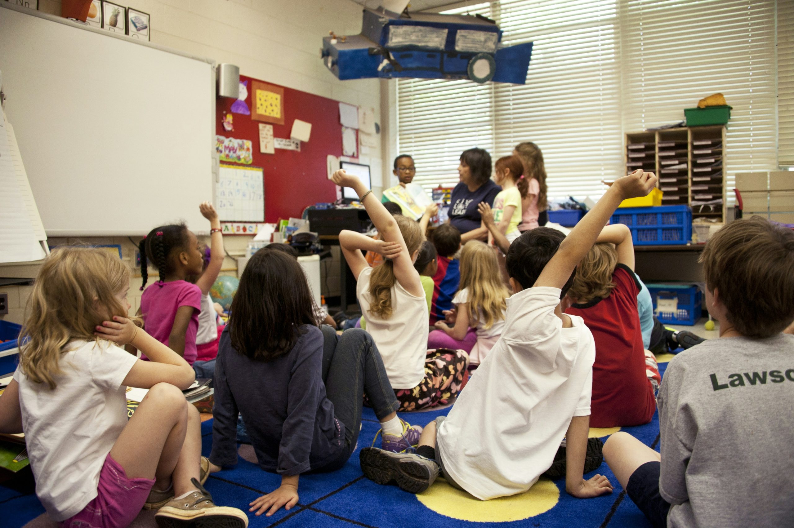 Students in an elementary classroom raising their hands during a lesson, representing Quebec's school and childcare system for newcomer families.